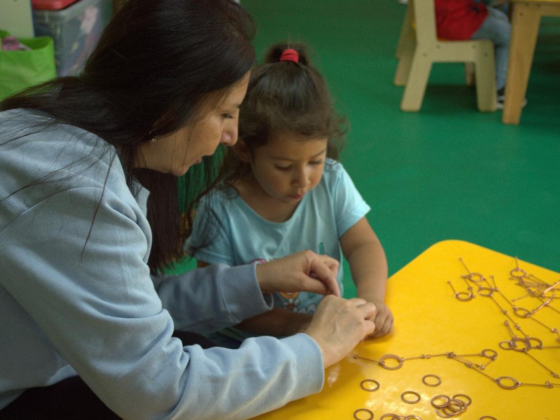 mujer le enseña a una niña, sentadas a una mesa